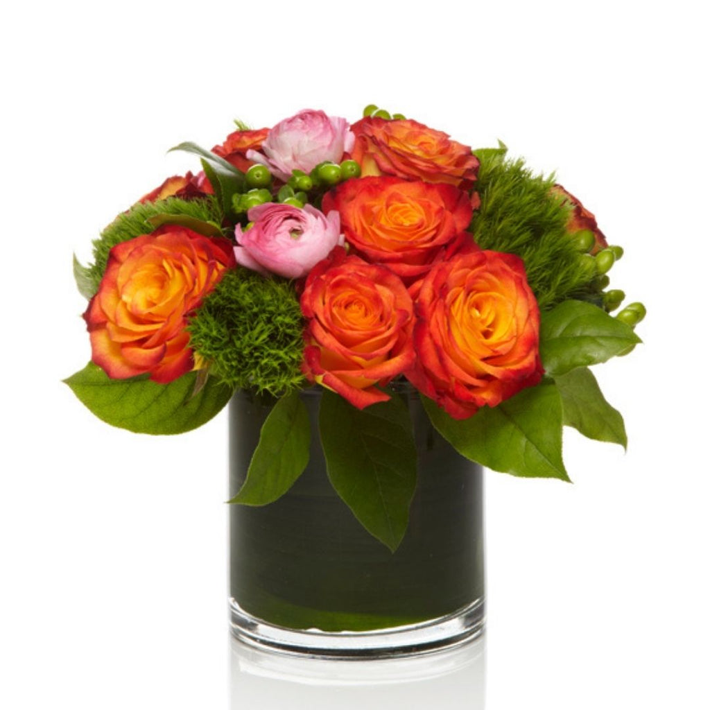 A bright arrangement of orange roses and premium pink seasonal blooms with modern greenery arranged in a chic glass vase.