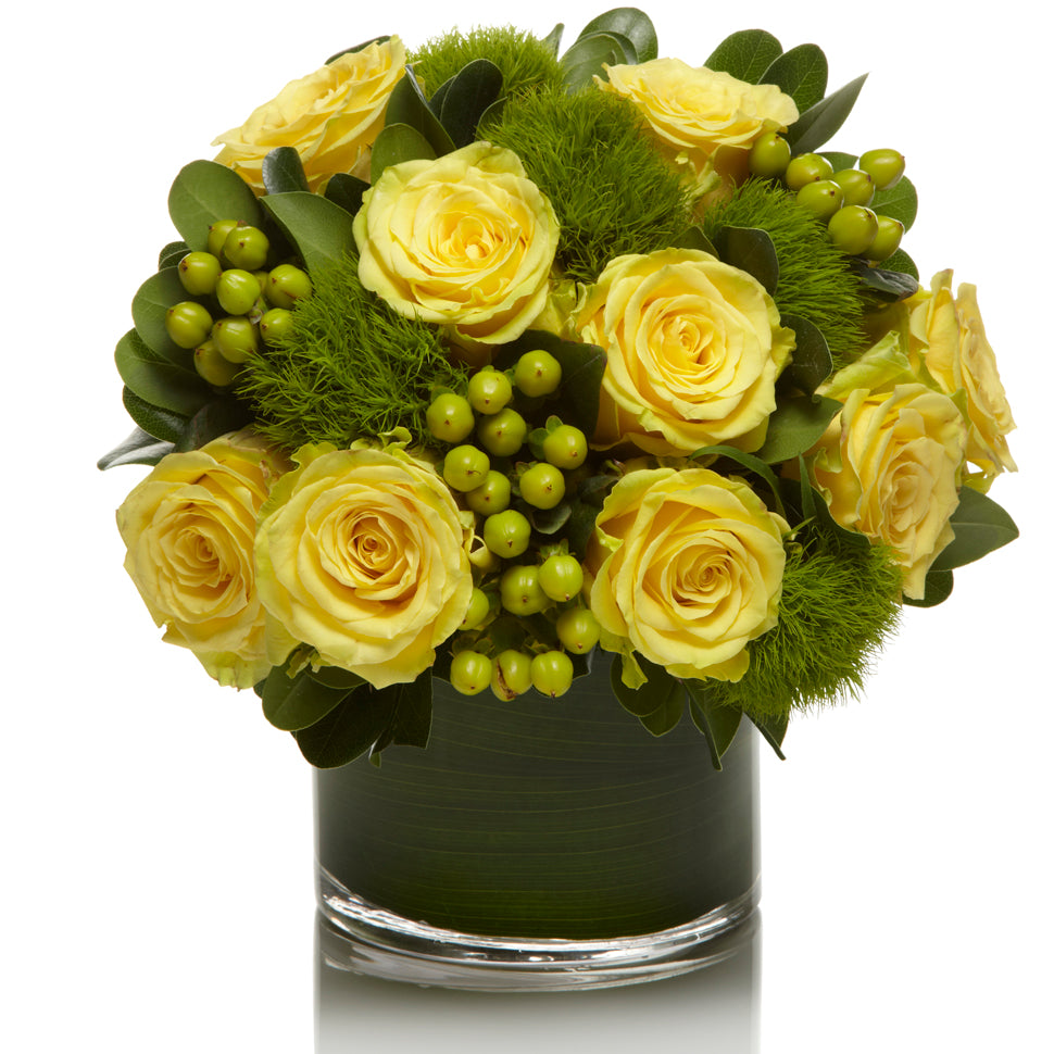 A modern mix of sunny yellow roses, green dianthus, and lime berries accented with greens in a chic glass vase.