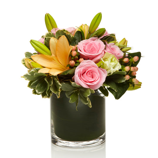 An arrangement of soft pink roses, orange lilies, and peach berries with a touch of greens