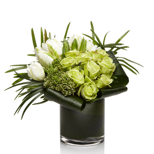 A luxe arrangement of soft green roses, white exotic blooms, and greens in a glass vase.