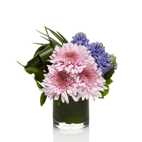 A cute mix of lavender mums and purple spring flowers arranged with modern greens.