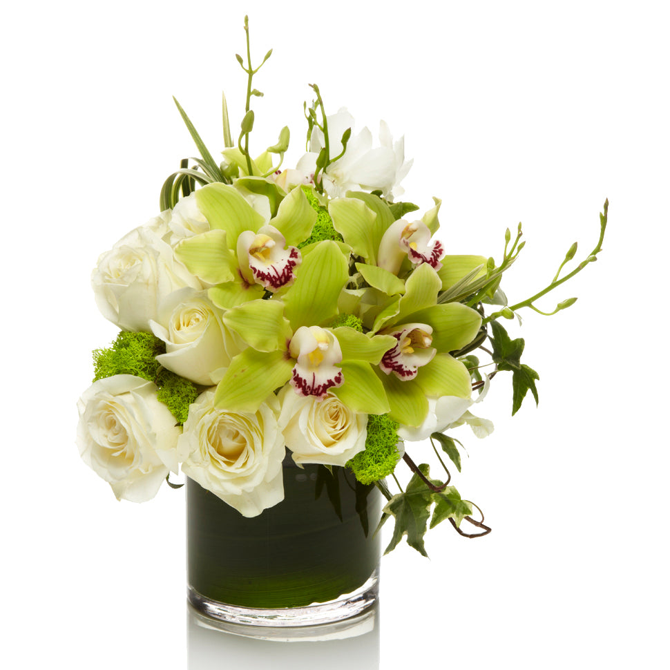 A fresh mix of white roses and lime cymbidium orchids with grass and accents of greenery in a glass vase.