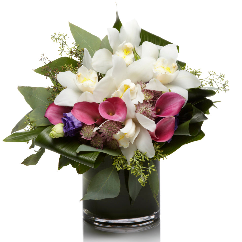 A beautiful mix of white orchids, pink calla lilies, and purple lisianthus accented with eucalyptus in a premium glass vase.