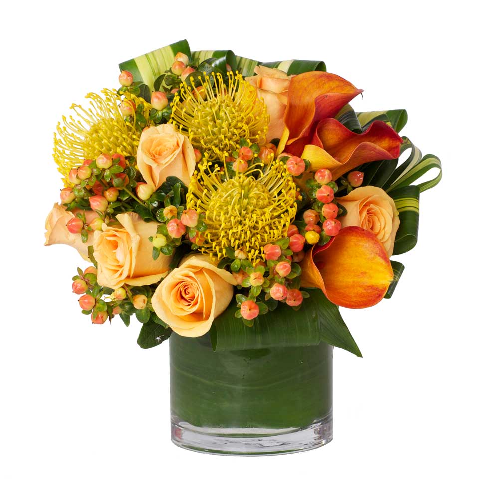 A vibrant mix of bright orange and yellow blooms such as roses, protea, and calla lilies accented with berries and modern greens.
