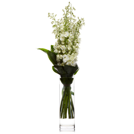 An arrangement of white delphinium or snapdragons, and seasonal white flowers accented with greens in a hurricane vase.